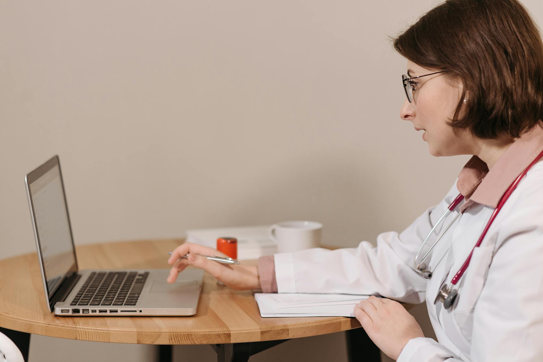 physician in white coat using her laptop