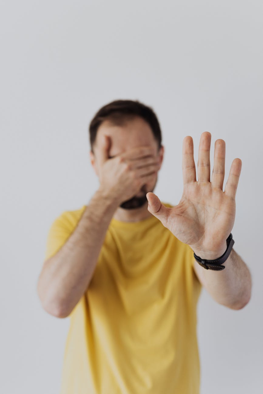 man covering his face with his hand and showing a stop sign gesture